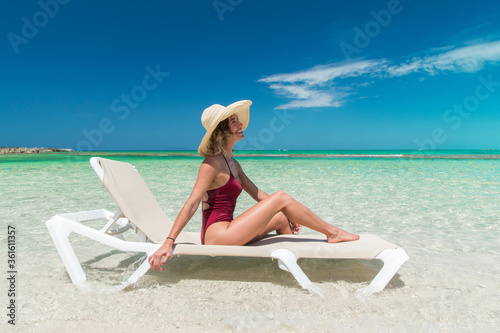 Summer vacation happy carefree joyful red bathing suit woman arms lounging in happiness enjoying tropical beach destination, sun hat, beach chair in tropical aqua lagoon, looking at sky