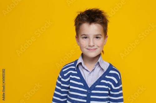 Portrait of a little cute smiling boy in a striped sweater isolated on a bright yellow background.