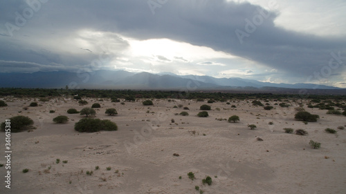 Desolated landscape. Aerial view of the sand, desert, flora and mountains under a dramatic sky and clouds at sunset. 