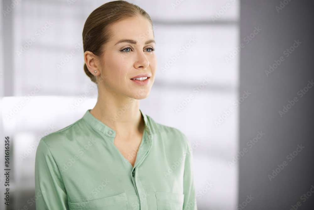 Beautiful adult business woman dressed in green blouse standing straight in office. Business headshot or portrait Beautiful adult business woman dressed in green blouse standing straight in office. Business headshot or portrait