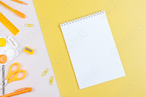 Concept back to school. School stationery flat lay: notepad with blank page, pens, pencils, sharpener, scissors, ruler, paper clips on yellow and gray background. Orange and yellow tones. Copyspace.