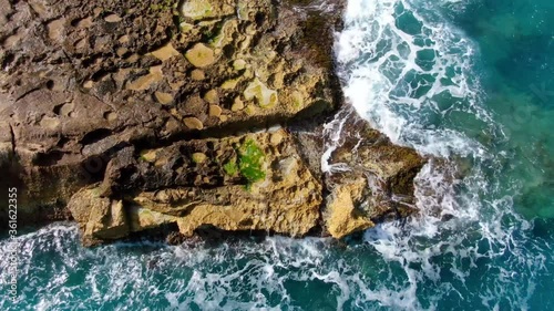 Wonderful turqouise blue ocean water hitting against the rocks - top down view photo