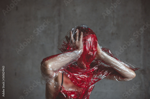 Screaming human face pressing through plastic stretch membrane painted red color. copy space
