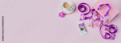 Flower overhead composition on light pink background top view. Cup of coffee, phone, pink gift shopping bag and purple orchid flowers.
