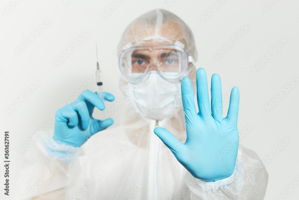 Stop virus. Male doctor in blue nitrile gloves, glasses and a respirator mask for protection holds a vaccine and syringe for injection. Coronavirus Vaccine concept. Stop virus. Male doctor in blue nitrile gloves, glasses and a respirator mask for protection holds a vaccine and syringe for injection. Coronavirus Vaccine concept.