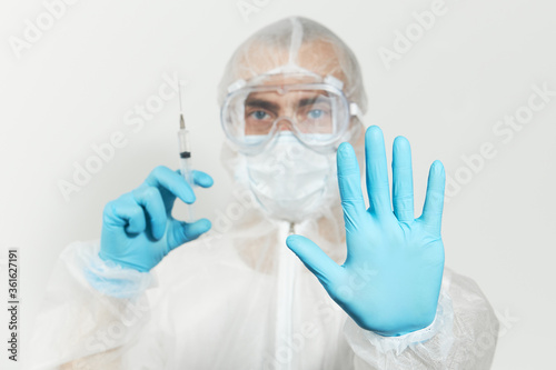 Stop virus. Male doctor  in blue nitrile gloves  glasses and a respirator mask for protection holds a vaccine and syringe for injection. Coronavirus Vaccine concept.