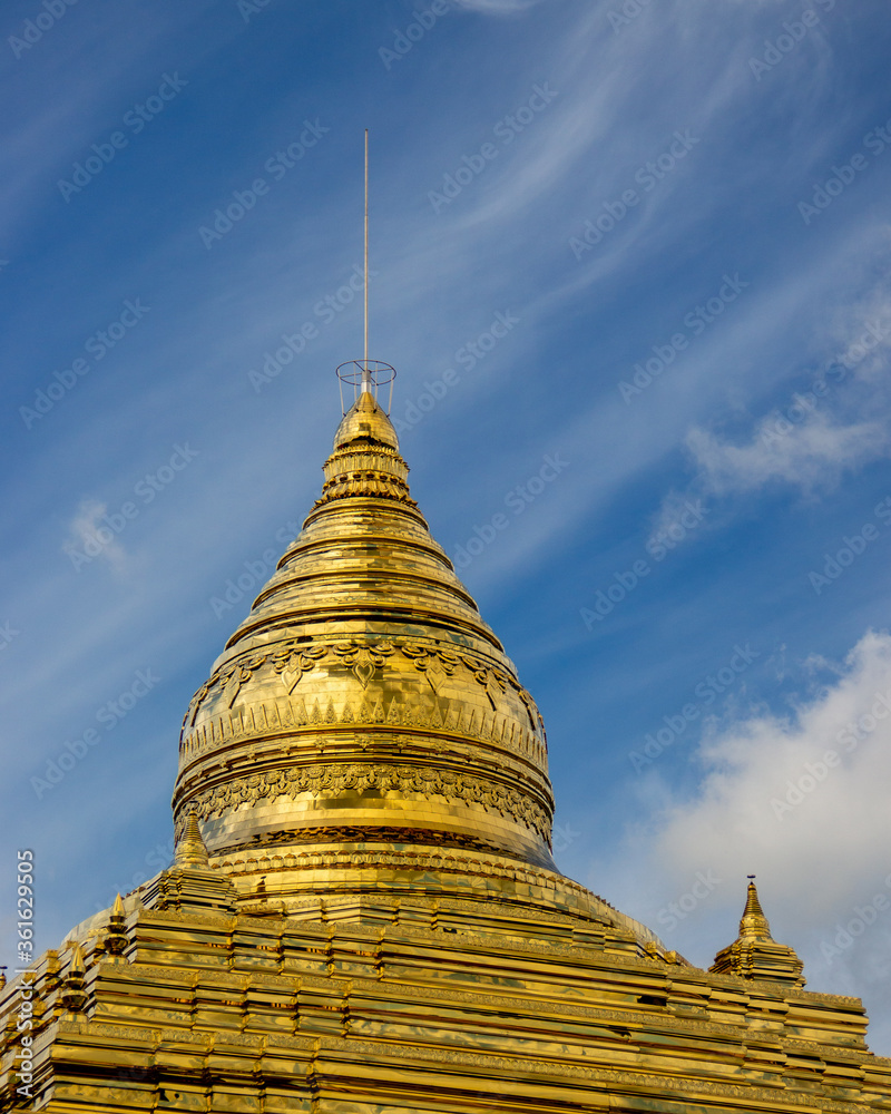 Fototapeta premium Golden Buddhist stupa on a background of blue sky with clouds