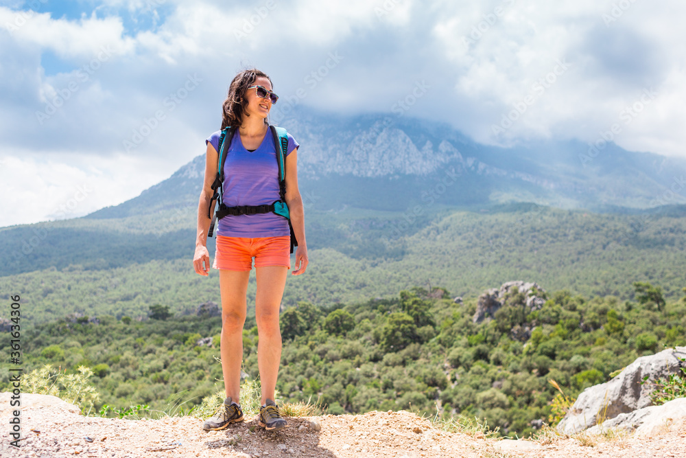 A woman with a backpack stands on top of a mountain and admires the beauty of a mountain valley. A woman with a backpack stands on top of a mountain and admires the beauty of a mountain valley.