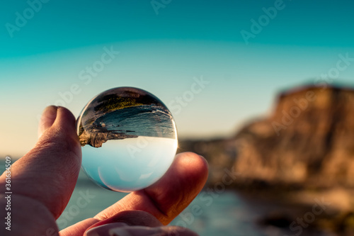 Porto Barril beach with selective focus through a lens ball reversing cliff by the sea with defocused background