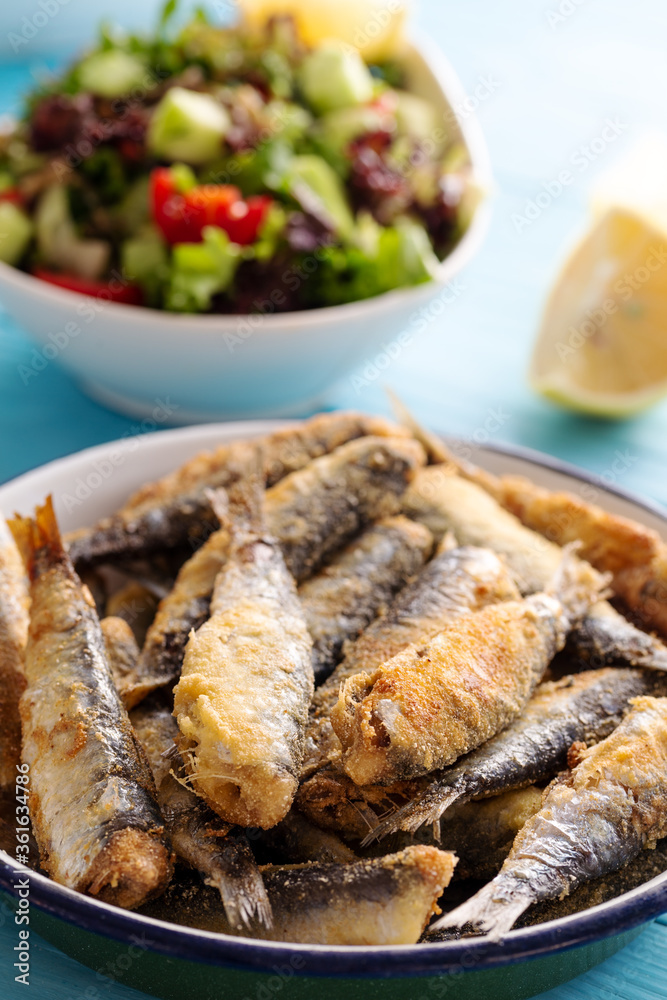 Fried sardines with lemon and salad on wooden background