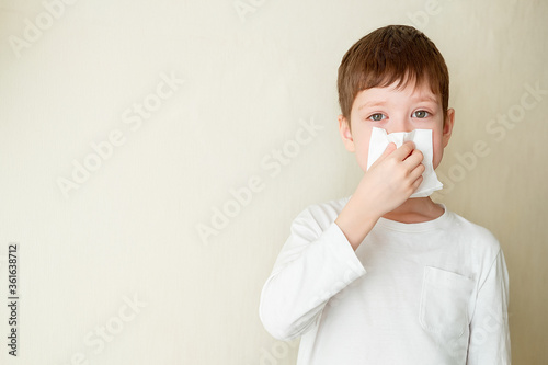 young boy blows his nose on a white background