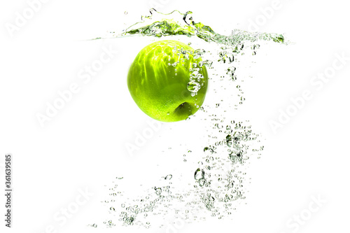 one green apple falling into water on a white background with splashes, drops and bubbles.