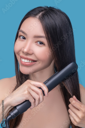 Smiling long-haired woman using a straightening iron