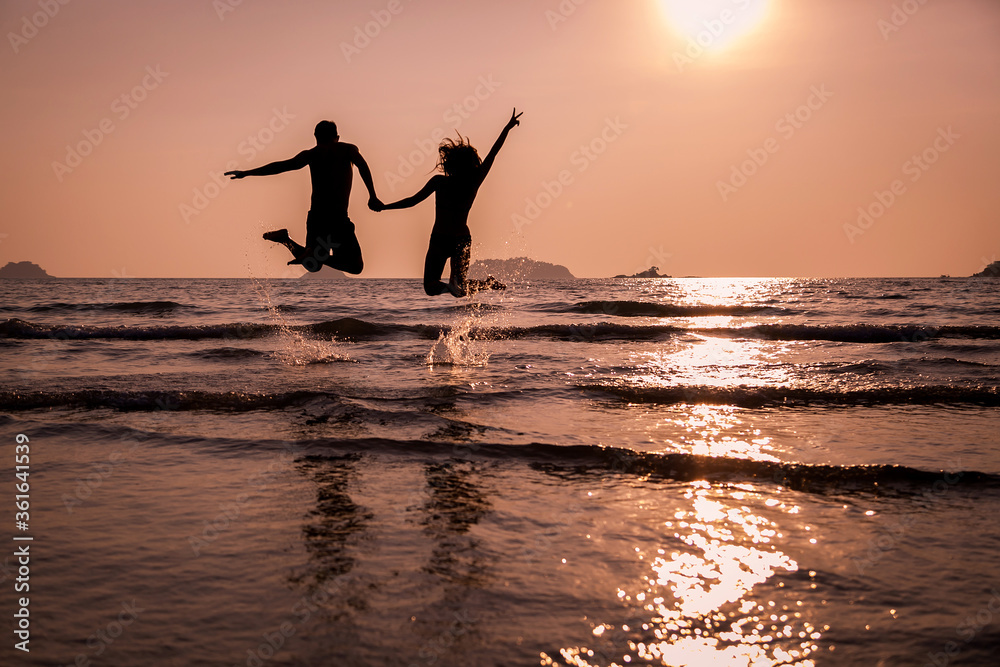 A pair of young people jumping into the sea. Silhouette at sunset.