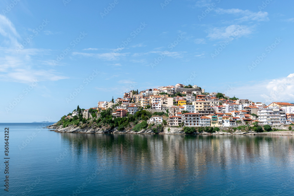 Colorful view of greek city of Kavala on sunny summer day. The old city and its reflection in calm sea. Northern Greece, Eastern Macedonia, Europe. Popular tourist destination. Copy space