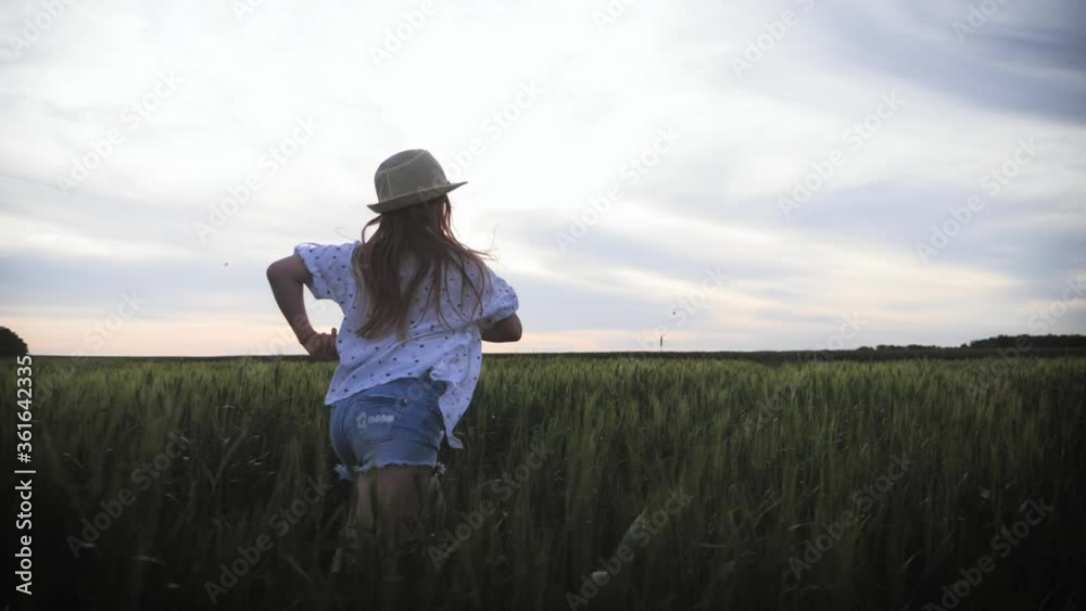 Pretty child in the hat is running across the wheat field. Happy young girl running in the field at sunset. Freedom concept. Pretty child in the hat is running across the wheat field. Happy young girl running in the field at sunset. Freedom concept.