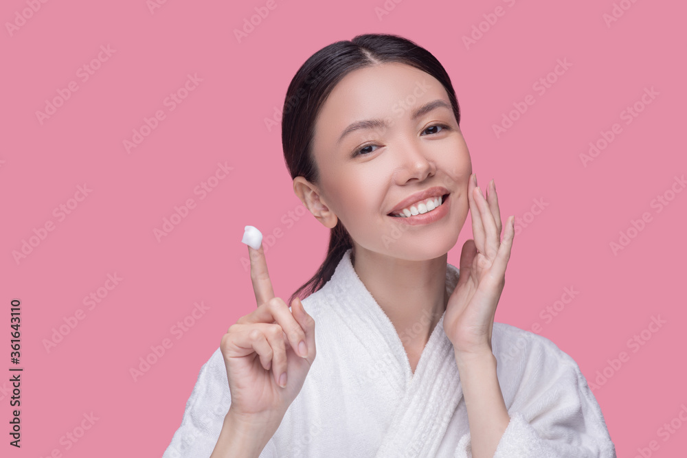 Smiling woman applying new face cream to her skin Smiling woman applying new face cream to her skin