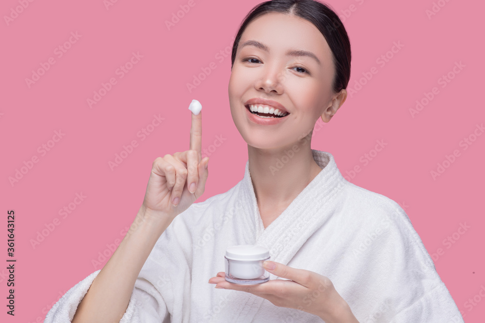 Smiling young woman applying nutrition cream to her skin Smiling young woman applying nutrition cream to her skin