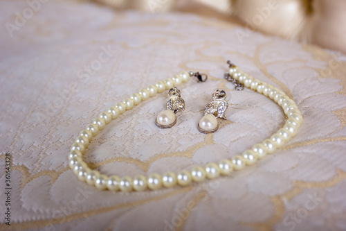 Pearl earrings lie on a bed surrounded by a pearl necklace against a beige bedspread vintage