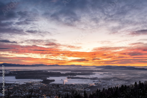Colorful sunrise over small town Kranj and mountains in the distance in wintertime, Slovenia. Elevated aerial view of landscape covered with snow photo
