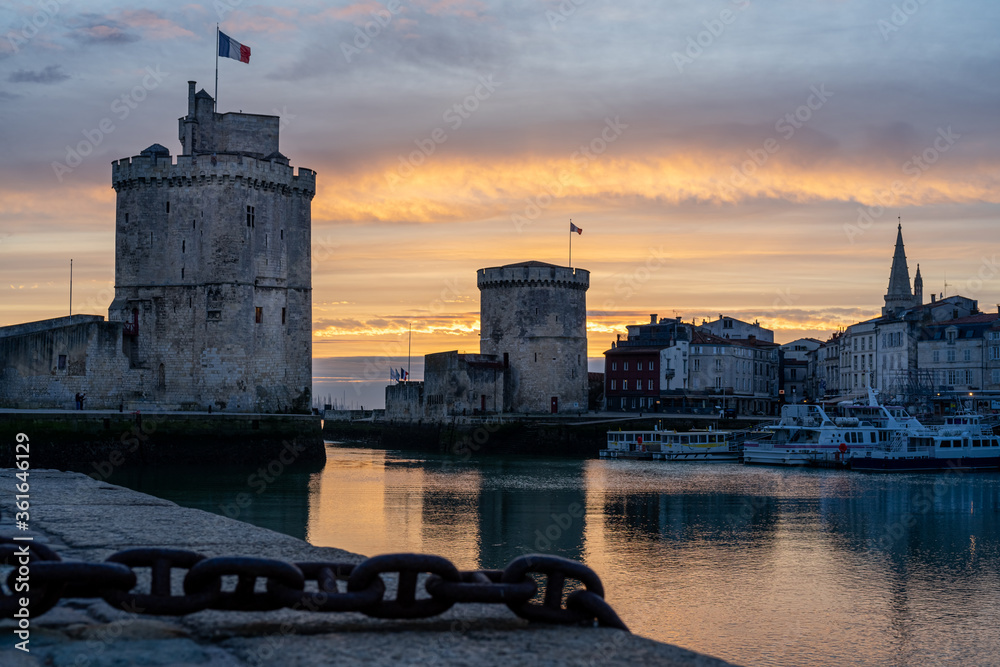The old harbor of La Rochelle at sunset with its famous old towers. beautiful orange sky. Chain on the foreground The old harbor of La Rochelle at sunset with its famous old towers. beautiful orange sky. Chain on the foreground