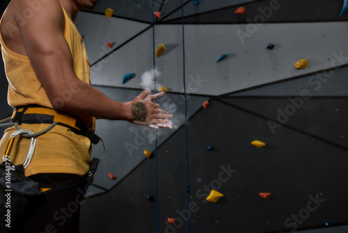 Obraz na plátne Cropped shot of sportive man applying white dust of magnesia, chalk on hands before climbing wall in bouldering center