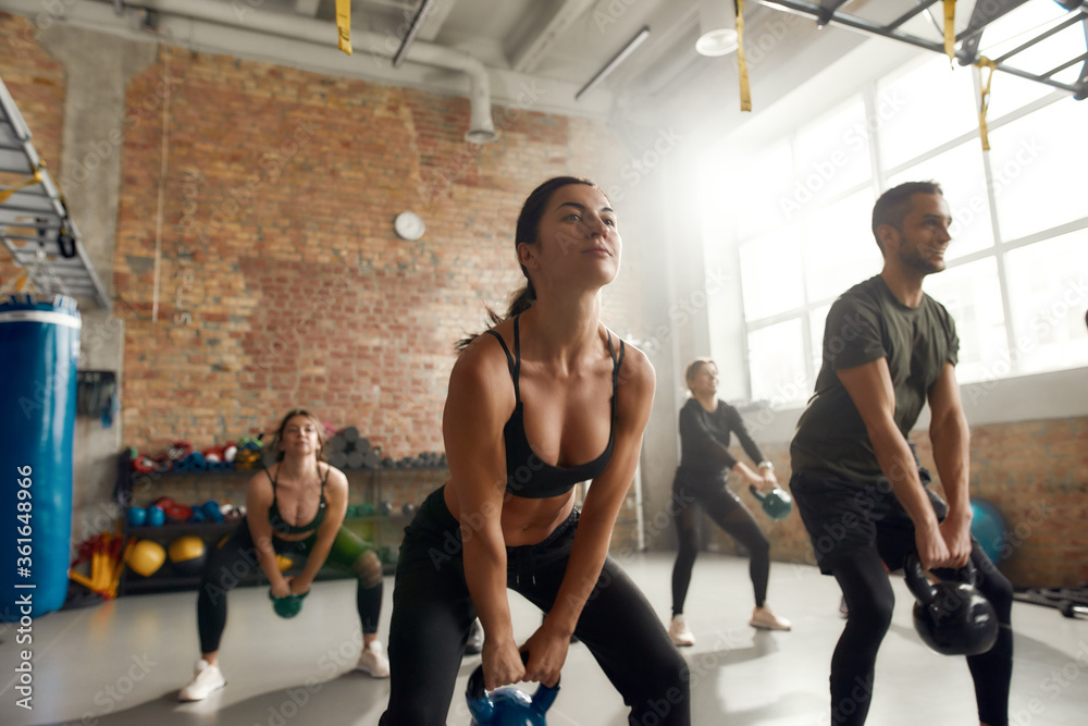 Obraz premium Get the toned body you dream of. Group of sportive people lifting weight while having workout at industrial gym. Group training, teamwork concept