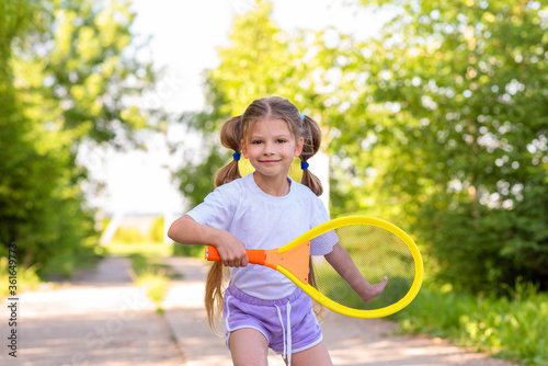 A little girl with two ponytails is playing tennis in a green Park.