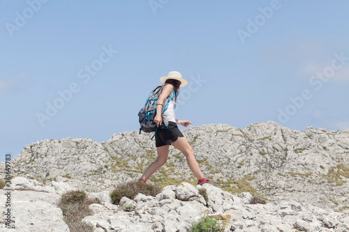Fit female hiker with backpack and hat during a trekking trip in the Tramuntana mountains in Mallorca. Concept of passion for travel. Backpacker. Outdoor summer lifestyle.