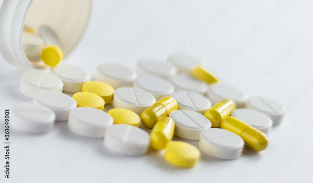 Jar and Pile of yellow and white capsules isolated on a white background. Medical concept