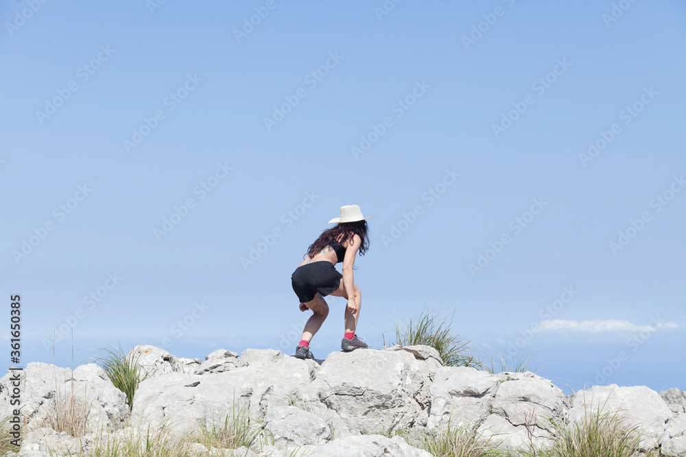 A girl traveling during the new normal of the summer holidays trekking through the mountains with views of the sky and the peaks, The girl is jumping with joy. Majorca island.