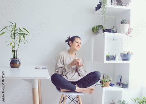 Hermosa mujer tomando café en la sala de estar. Mujer tomando café en la mañana en su casa. Mujer descalza sentada en una silla toma una bebida caliente mientras mira a la ventana. 