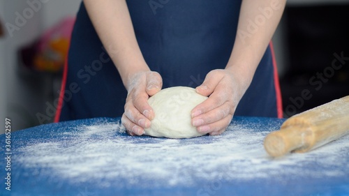 Manos de mujer amasa la masa cruda sobre una mesa azul. Panadero prepara masa para hacer pasteles, pizzas o pastas. photo