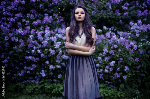 Fashion portrait of young beautiful pretty girl posing against lilac bushes in blossom