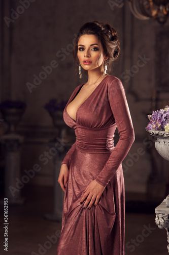 Murais de parede Young beautiful lady in evening dress posing in dark interior and looking at you