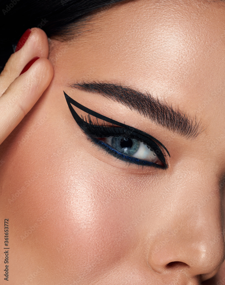 Naklejka premium Beautiful woman portrait with fresh daily make-up black hair and healthy skin. perfect eyeliner arrows. Eyebrows Care. Closeup Of Woman Beautiful Blue Eye, Perfect Shaped Brow, Long Eyelashes 