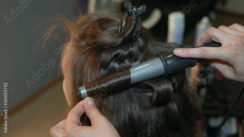 The hairdresser curls the hair of a girl in a beauty salon using a curling iron.