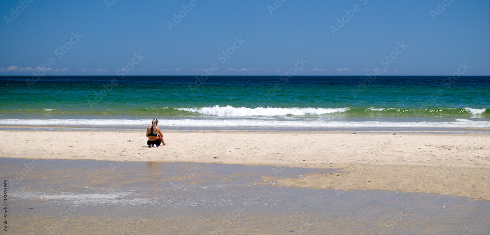 Mulher sentada numa praia virada de frente para o mar a descansar, relaxamento