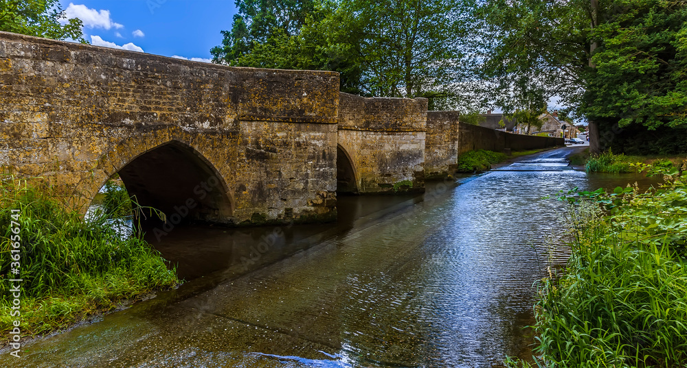 A view towards the eighteenth-century bridge and ford over the River Ise in the town of Geddington, UK in summer