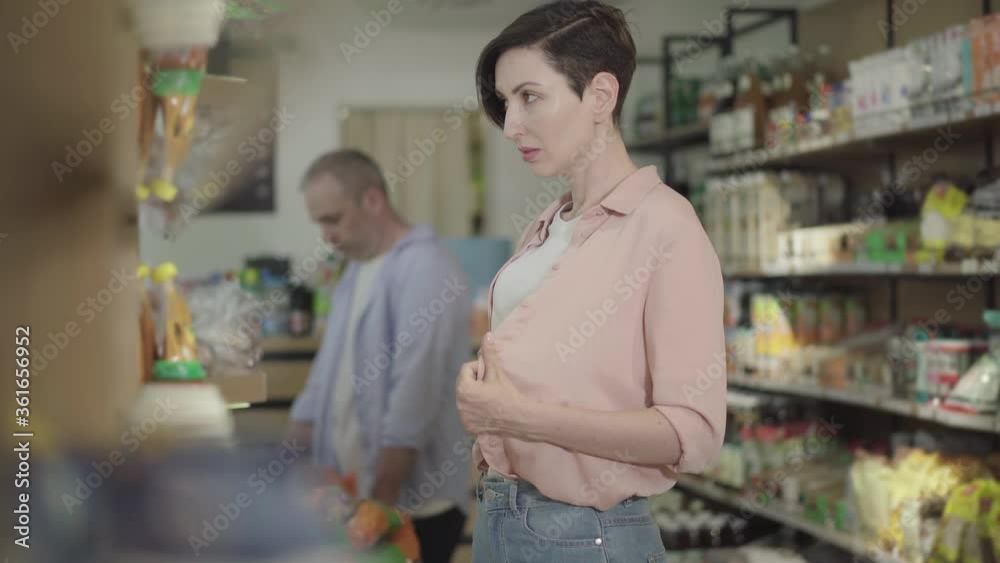 Young attractive woman looking around in grocery and stealing packaging of cookies. Portrait of female robber violating law in food shop. Crime, burglary, robbery, lifestyle. Young attractive woman looking around in grocery and stealing packaging of cookies. Portrait of female robber violating law in food shop. Crime, burglary, robbery, lifestyle.