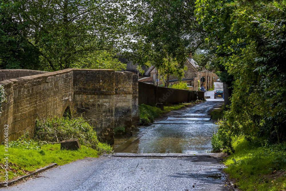 A view towards the southern part of town across the bridge and ford in the town of Geddington, UK in summer