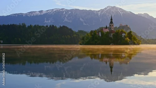 Beautiful morning at Lake Bled and Julian Alps in the background. The lake island and charming little church dedicated to the Assumption of Mary are famous tourist attraction in Slovenia.