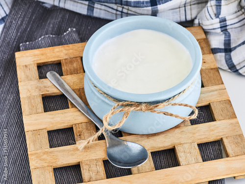 Close up on Greek yogurt in a ceramik blue bowl with a spoon on a wooden stand, rustic style photo