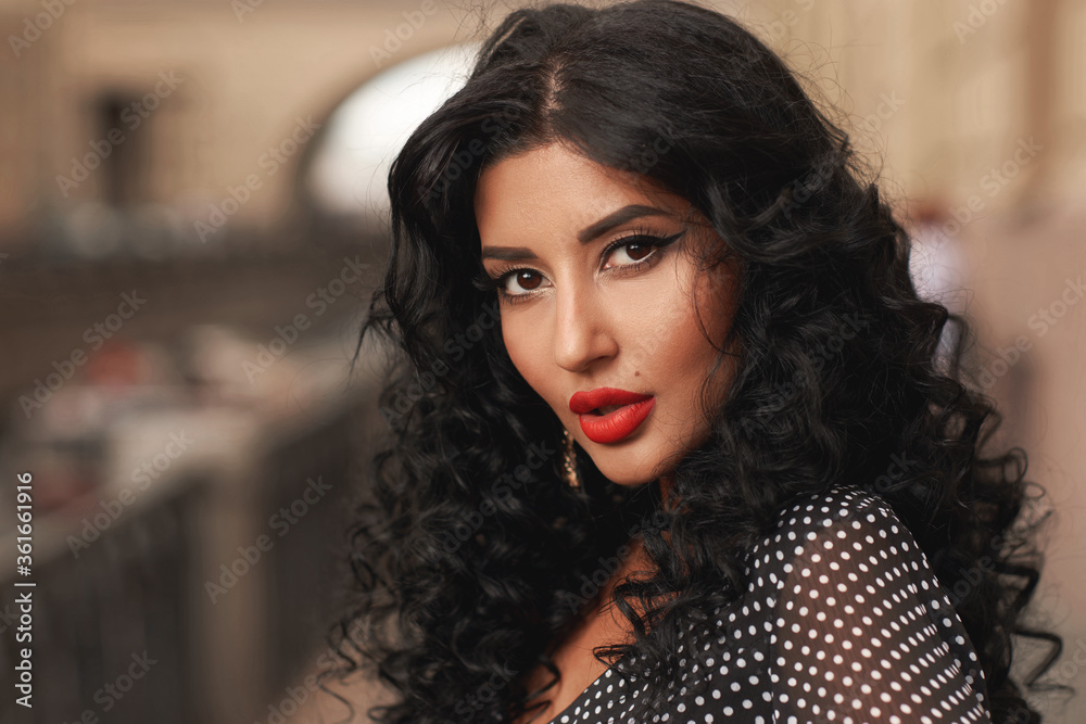 Outdoor closeup face portrait of young brunette woman with afro curly hair, makeup and red lips. Fashion style shot. Elegant girl in black and white polka dot dress Outdoor closeup face portrait of young brunette woman with afro curly hair, makeup and red lips. Fashion style shot. Elegant girl in black and white polka dot dress