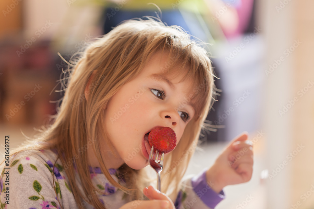 Adorable little girl in pajama eating strawberries at home