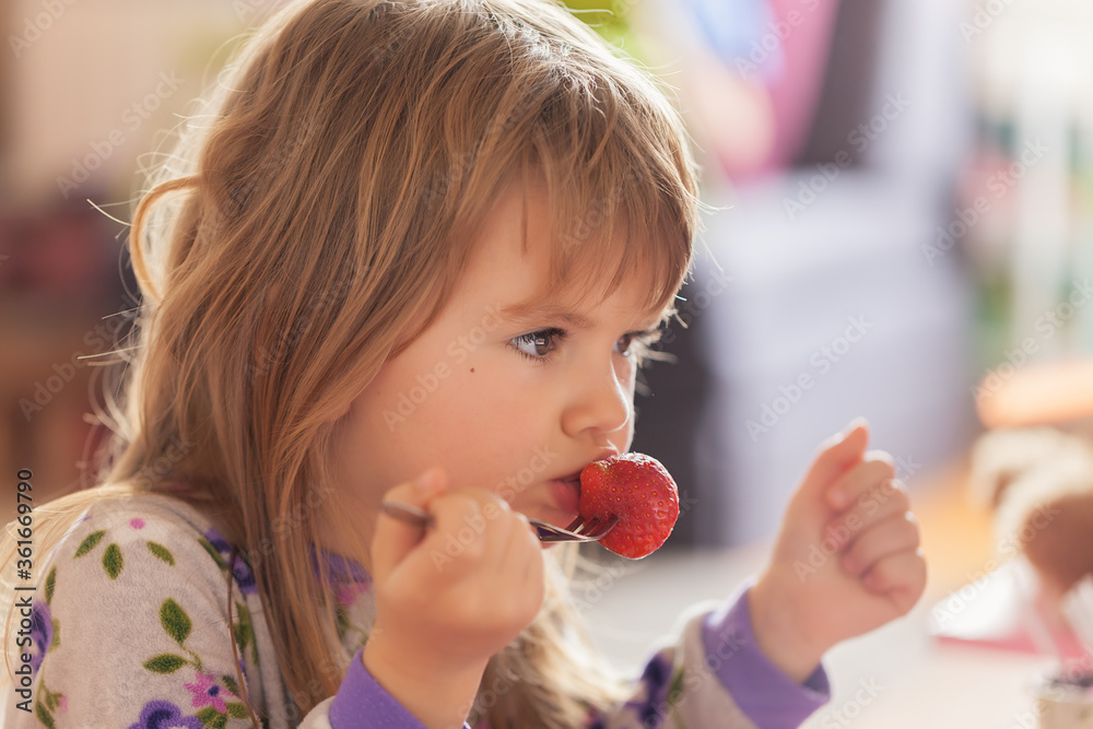 Adorable little girl in pajama eating strawberries at home Adorable little girl in pajama eating strawberries at home