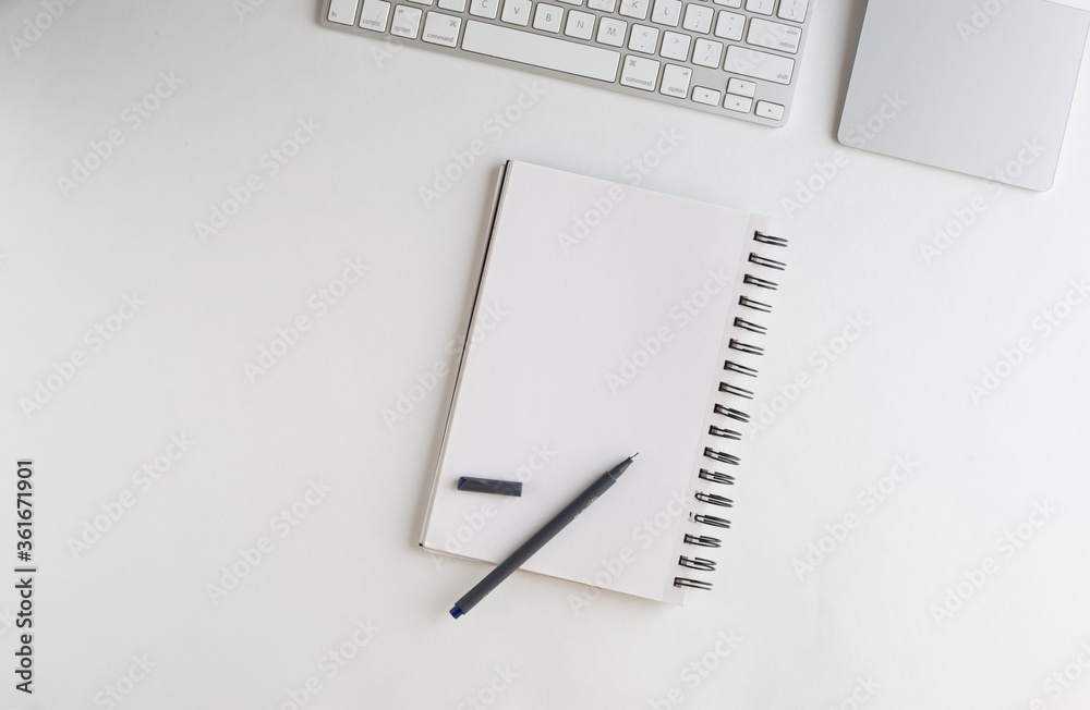 Keyboard, trackpad, notebook and a pen on white background suggesting clean office desk space Keyboard, trackpad, notebook and a pen on white background suggesting clean office desk space