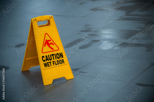Yellow wet floor caution sign during rain with a puddle of water when the floor is slippery and copy space for text
