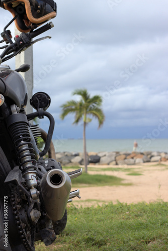 Focused view of the rear end of an antique motorcycle fading to the view of the beach