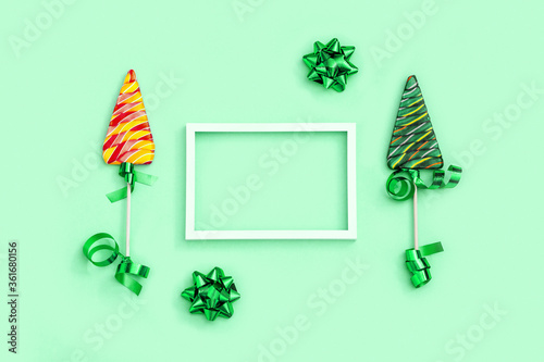 Color candy creative for New Year or Christmas. Lollipops shaped like Christmas tree and and white frame with copy space on neo mint colored paper background. Top view. photo